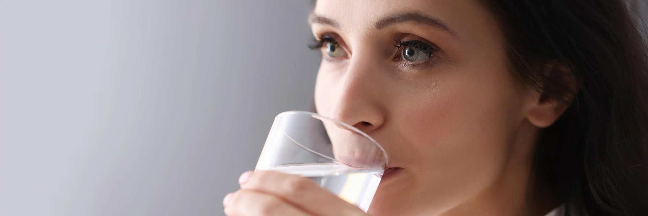 Young brunette woman drinking water from glass to stay hydrated.