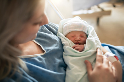 Happy woman after giving birth, holding the healthy baby in her hands.