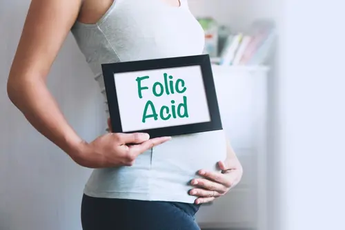 Pregnant woman holding an image, on which is written Folic Acid.