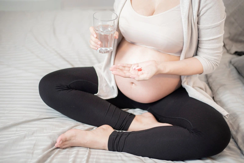 Pregnant woman sitting on her bed and taking her daily dose of vitamins.